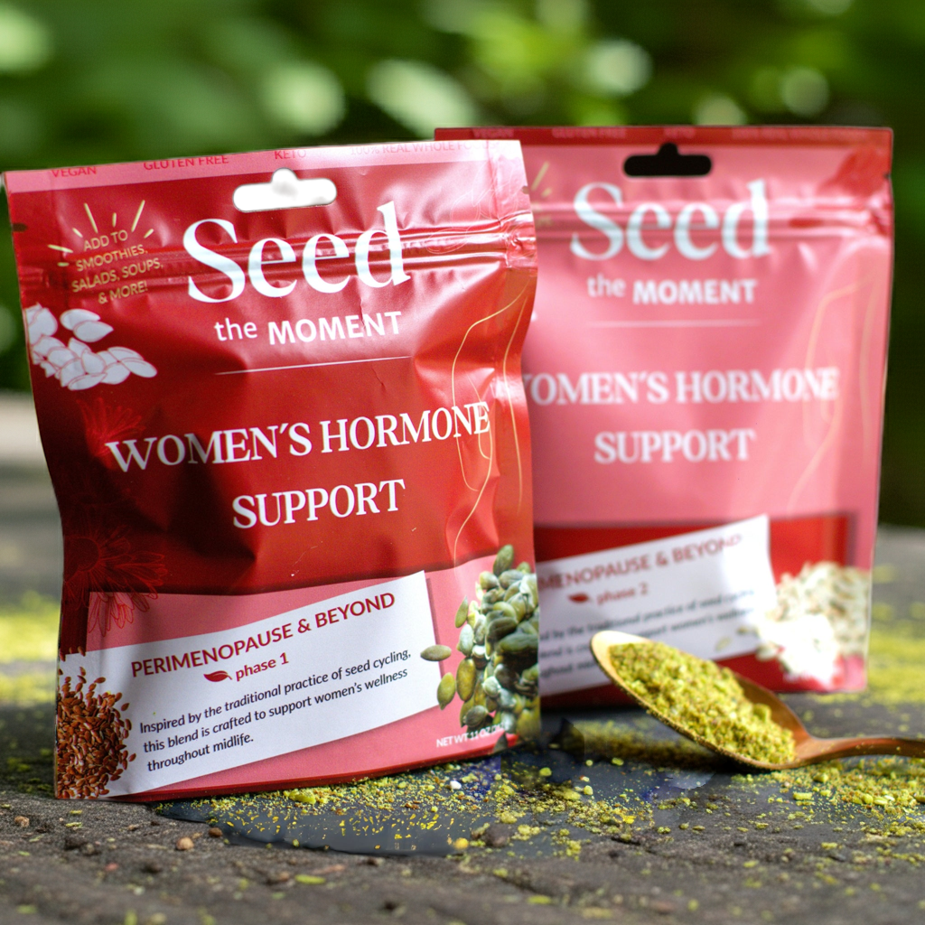 bags of seed the moment hormone support with a green leafy background and a spoonful of seeds.